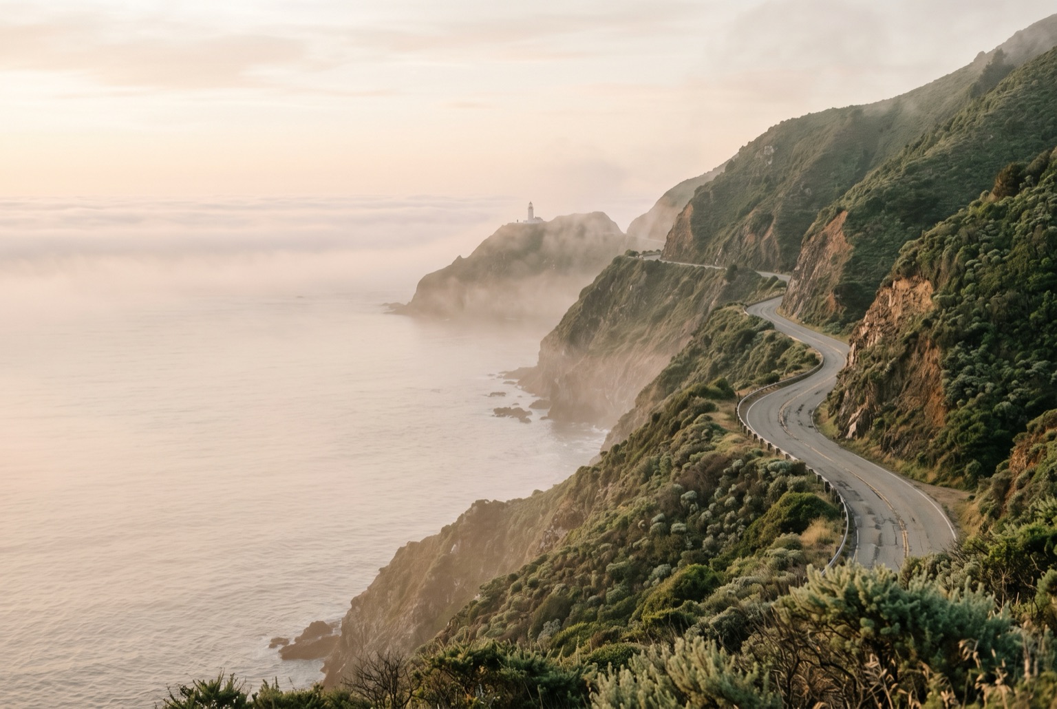 A coastal road and a lighthouse in the morning mist